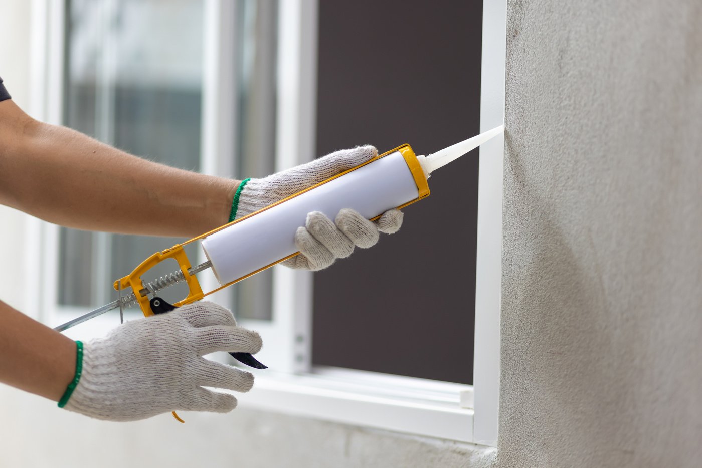 Construction worker using silicone sealant caulk the outside win